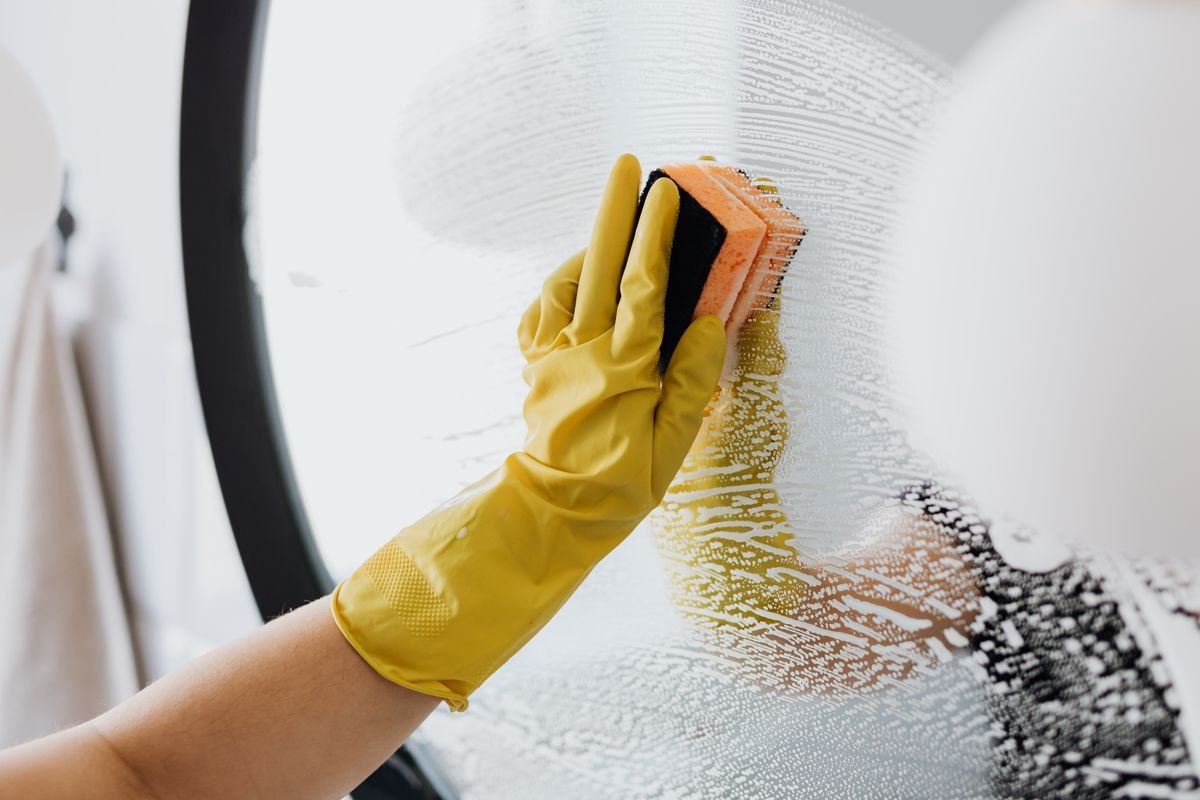 Gloved hand cleaning a bathroom mirror with a sponge